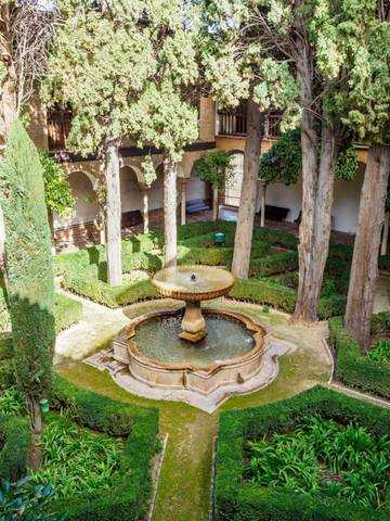 Fuente en el jardín de los Palacios Nazaríes de la Alhambra, rodeada de árboles y setos cuidados, representativa de la arquitectura y naturaleza en Granada